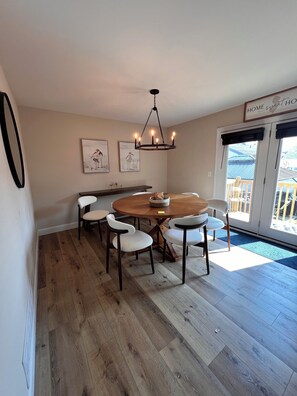 A dining area with a round table, six chairs, and a hanging light fixture.