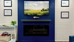 Un salon avec un téléviseur fixé au mur bleu, une cheminée en dessous et des œuvres d’art encadrées qui décorent les murs.