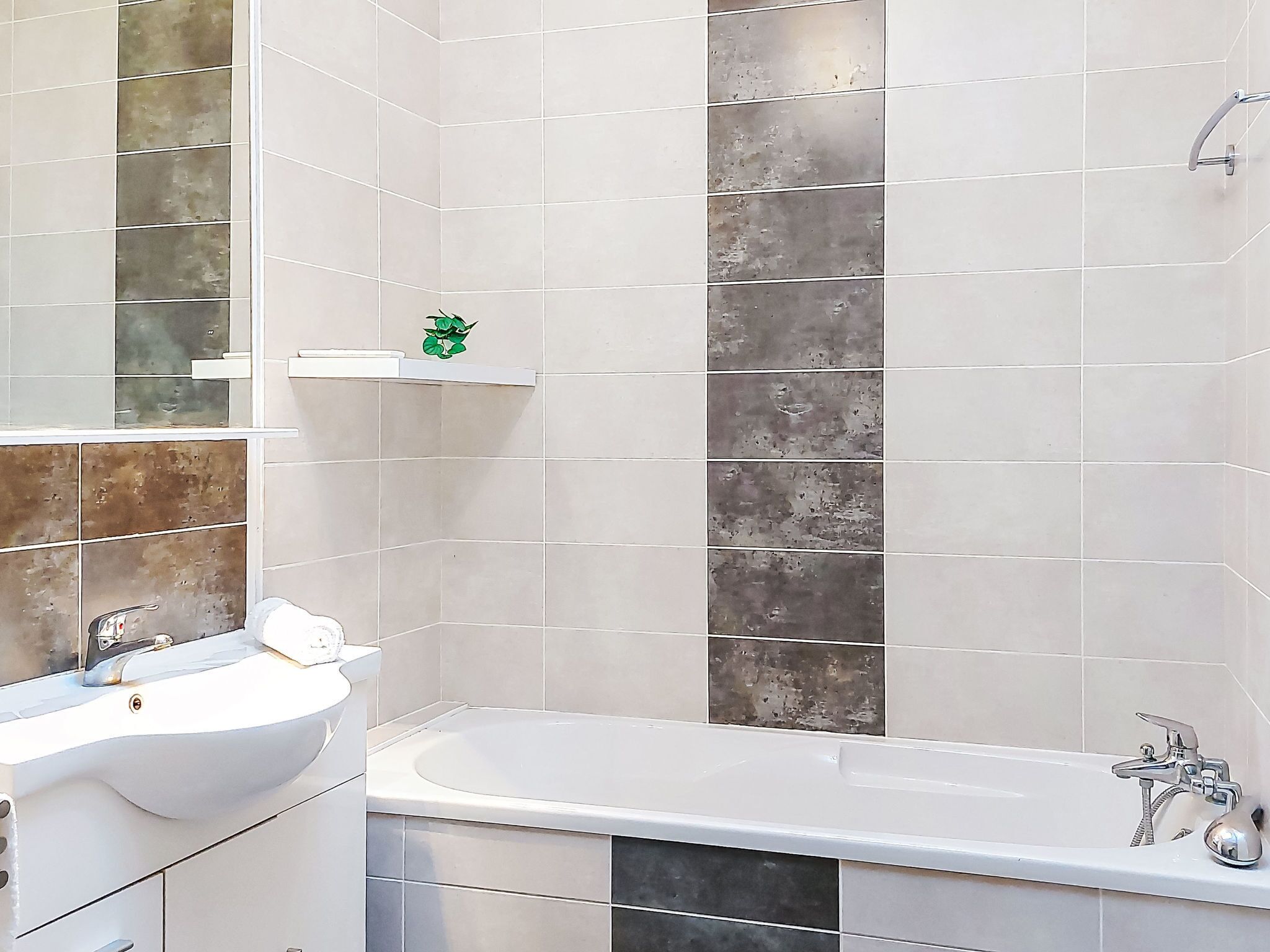 A bathroom with a white sink, a bathtub, and a shower. There is a shelf with a green object on it.