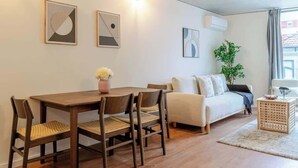 Een moderne woonkamer met een houten eettafel, twee stoelen, een bank en een bijzettafeltje.