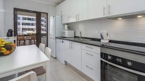 Uma cozinha moderna com armários brancos, bancada preta, forno embutido e um espaço de jantar com mesa e cadeiras brancas.