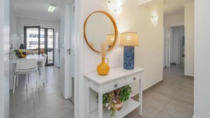 Um corredor moderno com uma mesa consola branca, espelho, um vaso amarelo e um vaso azul com uma planta.