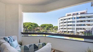 Varanda com sofá, uma mesa pequena e vista para uma piscina e edifícios.