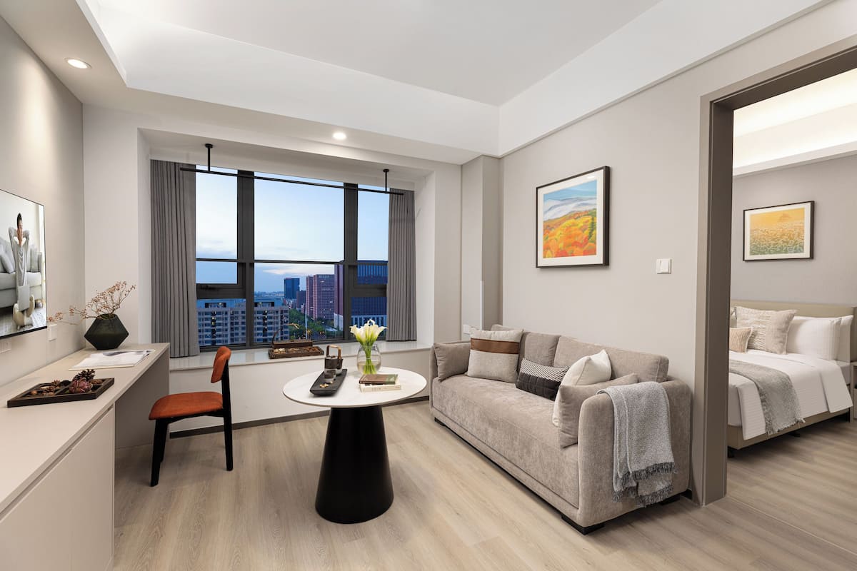 A modern living room with a sofa, a dining table, and a view of the cityscape through large windows.