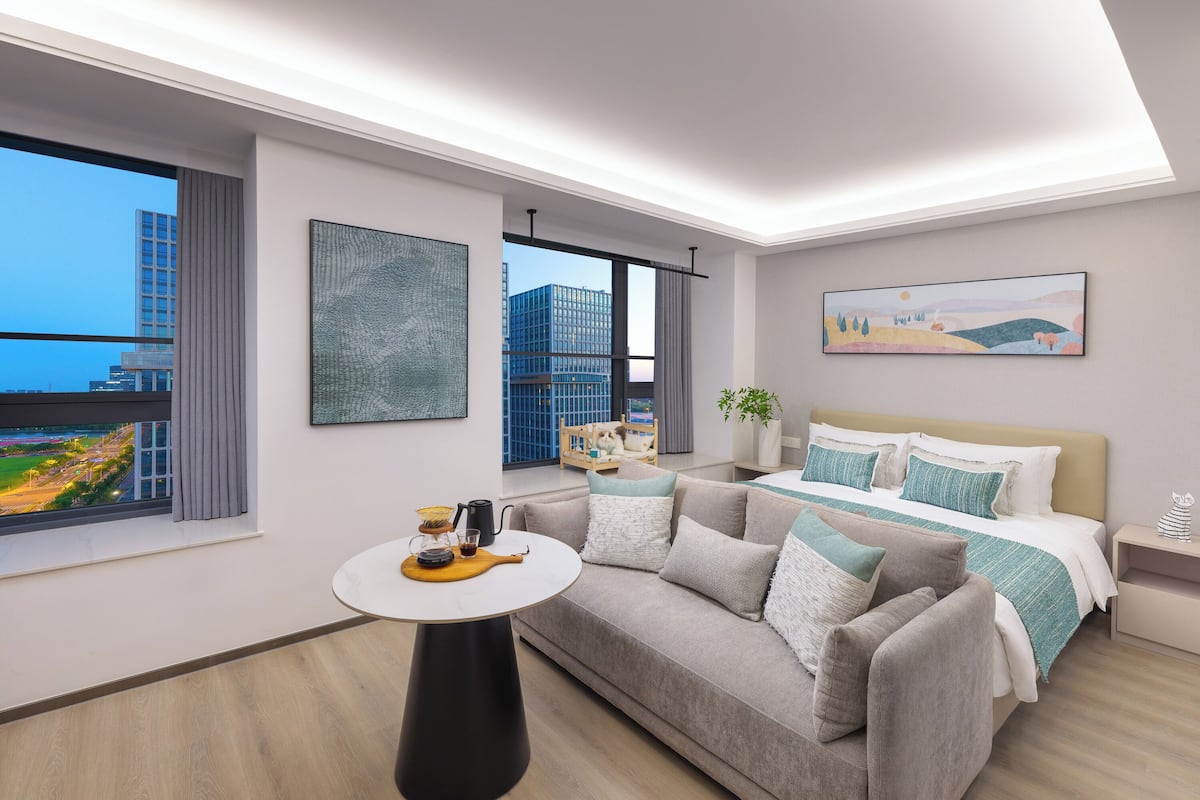 A modern hotel room with a large bed, a sofa, a small table with a tray, and a city view.