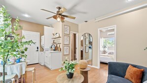 Un salon moderne avec un ventilateur de plafond, un coin repas avec une table et des chaises, et une cuisine en arrière-plan.