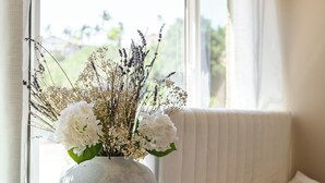 Une chambre avec un lit, une fenêtre avec des rideaux et un vase de fleurs sur une table de chevet.
