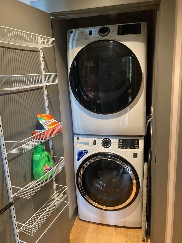 A laundry area with two stacked washing machines and a metal shelf with laundry detergent.
