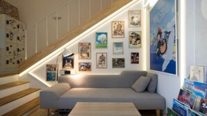 Un salón moderno con un sofá gris, una escalera de madera y una pared decorada con diversas obras enmarcadas.