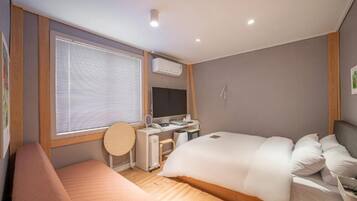 Een slaapkamer met een bed, een bureau, een stoel, een raam met jaloezieën en een airconditioning.
