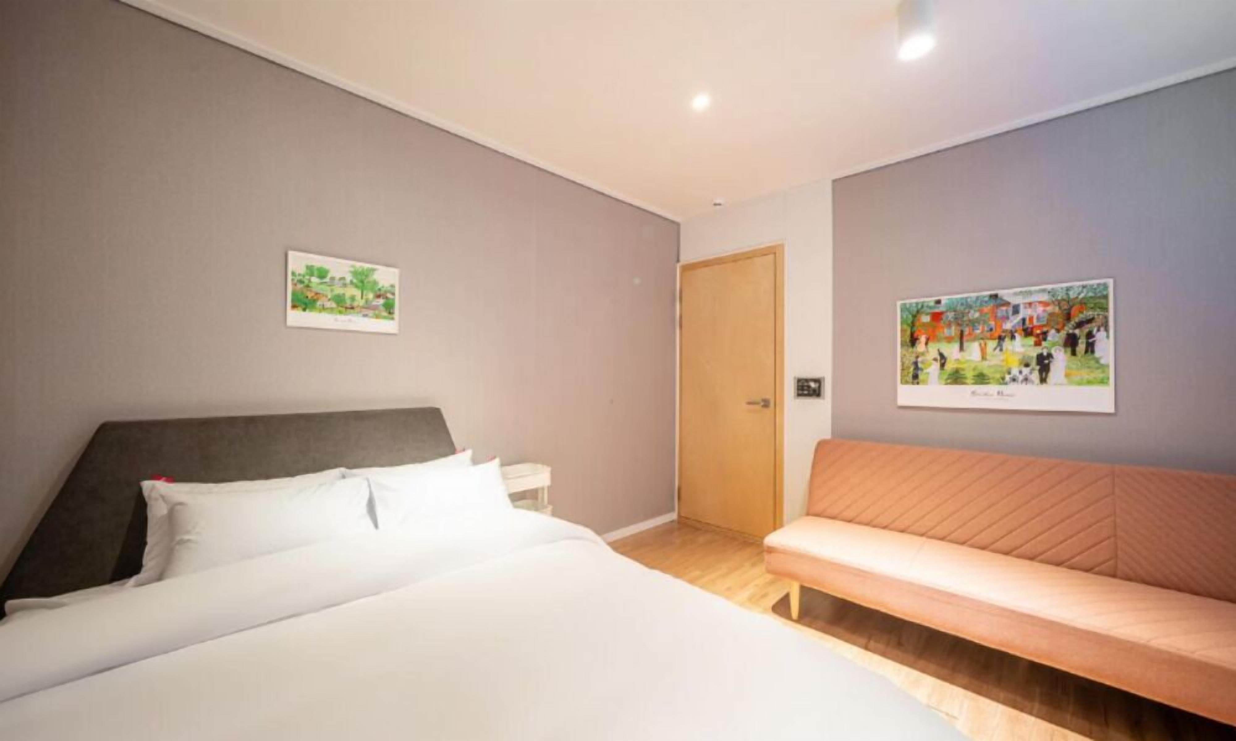 Un dormitorio con una cama, una mesita de noche, un banco y dos cuadros colgados en la pared.