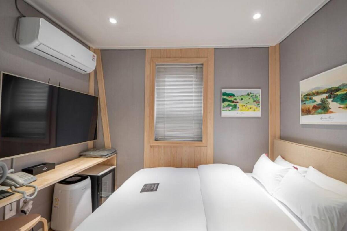 A hotel room with a bed, a desk with a computer, a TV, and a window with blinds.