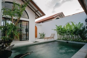 A modern house with a swimming pool, a wooden chair, and lush greenery. - Avura Villa Munggu (Munggu)