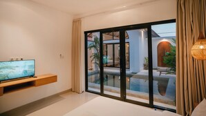 Ein modernes Wohnzimmer mit einem Flachbildfernseher auf einem Holzregal, großen Schiebeg lass-Türen, die zu einem Poolbereich führen, und einer hängenden Pendelleuchte.