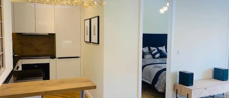 A compact living space with a kitchenette, a bed with a blue headboard, and a modern chandelier.