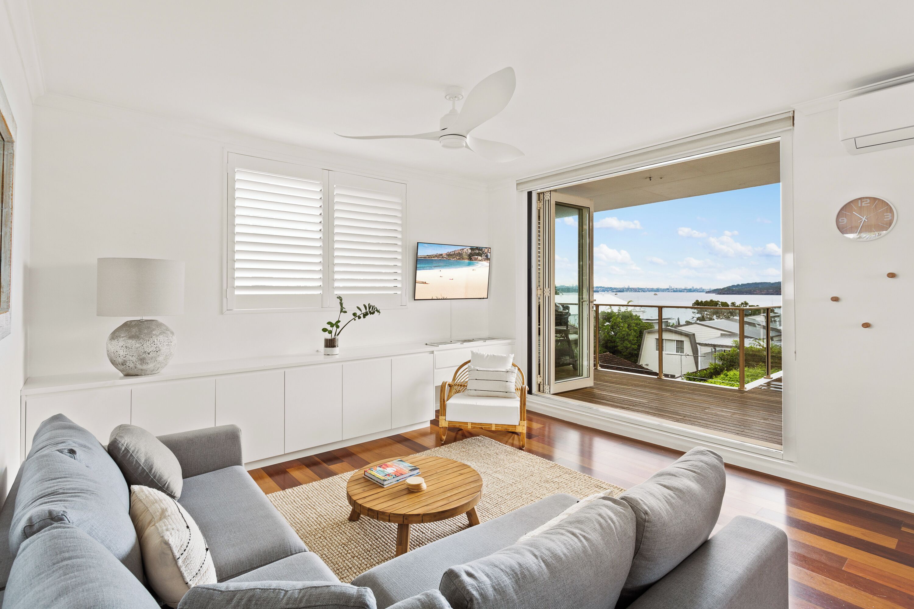 A modern living room with a sofa, a coffee table, a view of the sea, a dining area, and a balcony.