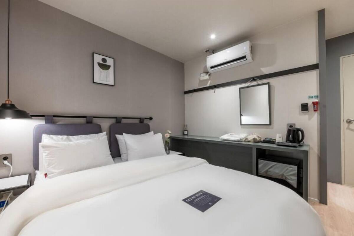 Une chambre d’hôtel comprenant un lit, des tables de chevet, un bureau, un appareil de climatisation, un miroir et une porte.