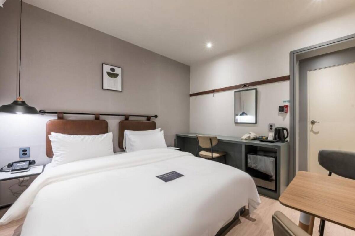 Une chambre d’hôtel avec un grand lit, un bureau avec une chaise, une petite table, un miroir et une porte.