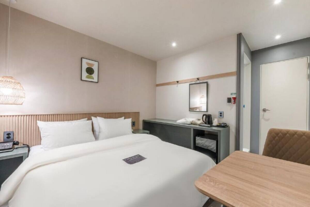 Une chambre d’hôtel équipée d’un lit, d’une table de chevet, d’une chaise, d’un bureau et d’un miroir fixé au mur.