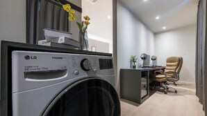 A modern laundry room with an LG TROMM 15kg DD Inverter washing machine, a desk with a computer, headphones, and a chair. - POHANG MANSION 6 HOTEL (Pohang)