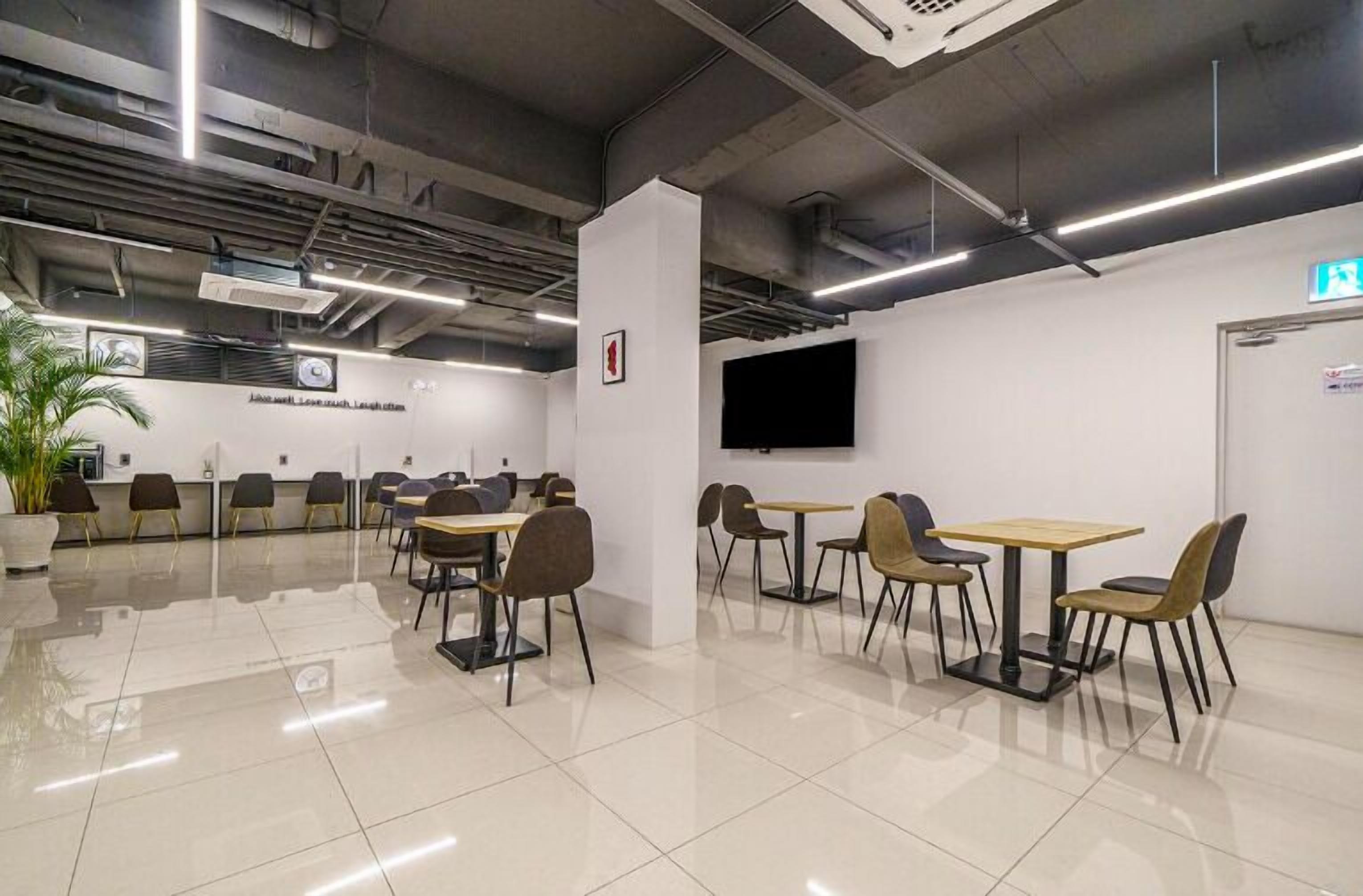 Un ambiente interno moderno con diversi tavoli e sedie, un televisore a schermo piatto montato a parete e una pianta in vaso.