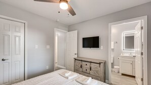 A bedroom with a bed, a ceiling fan, a dresser, a television, and a bathroom with a mirror and sink. - Country cozy with beach bless (Bolivia)