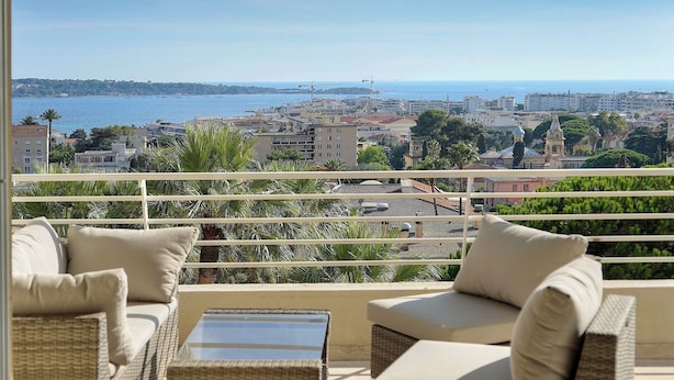 A balcony with wicker furniture and a view of the sea and cityscape.