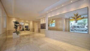 A spacious lobby with a polished marble floor, a reception desk, and a large mirror reflecting the interior.