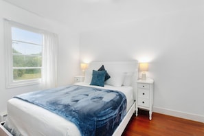 A bedroom with a bed, white nightstands, and a window with curtains. - The Bee House, Newly Remodeled (Grayland)