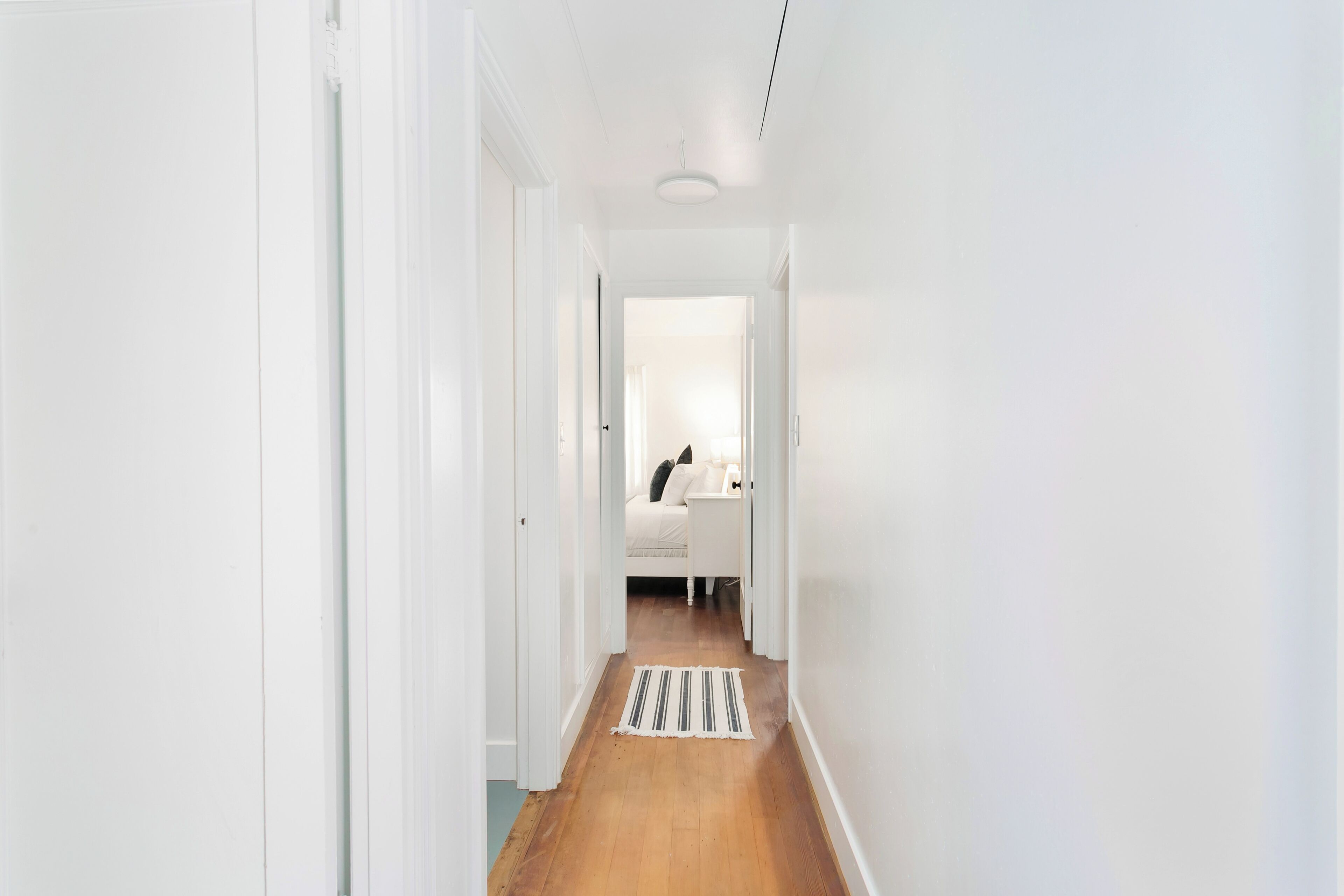 Un couloir étroit, doté d’un plancher en bois, mène à une chambre à coucher qui contient un lit et une table de chevet.