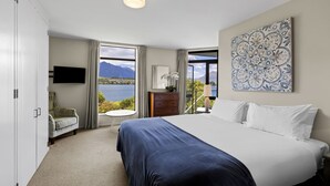 Une chambre avec un grand lit, une commode, une chaise, un téléviseur et une vue sur un lac et des montagnes.