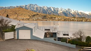 Une maison moderne avec un garage, un escalier menant à l’entrée et une vue sur un lac, avec des montagnes en arrière-plan.