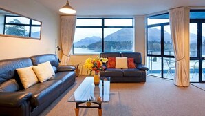 A living room with a sofa, a coffee table, and a view of mountains through large windows.