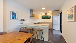 A modern kitchen with a wooden dining table, bar stools, and a refrigerator.