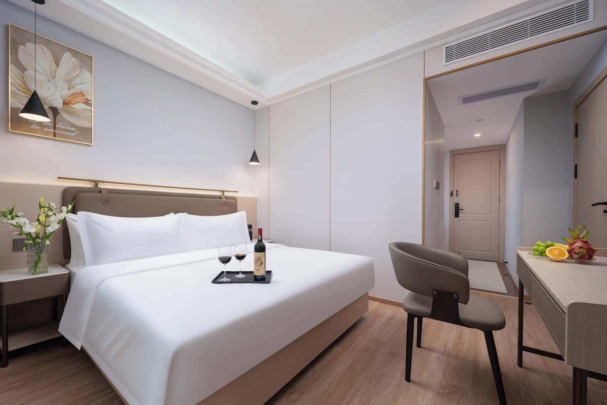 Habitación de hotel moderna con una cama grande, mesita de noche con un florero, un escritorio con una silla y un frutero.