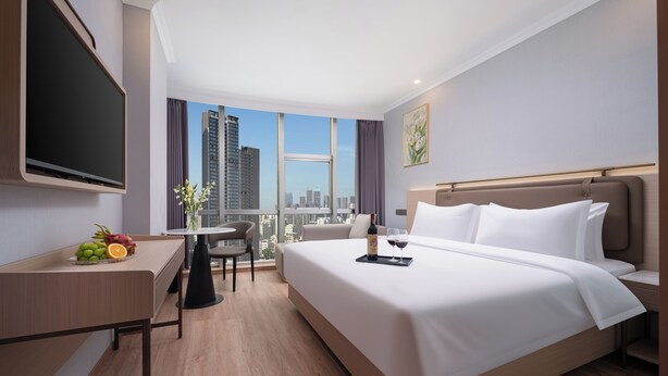 A hotel room with a large bed, a desk with a flat-screen TV, a dining area, and a city view. - Shenzhen Nanshan Yuetu Hotel (Shenzhen)