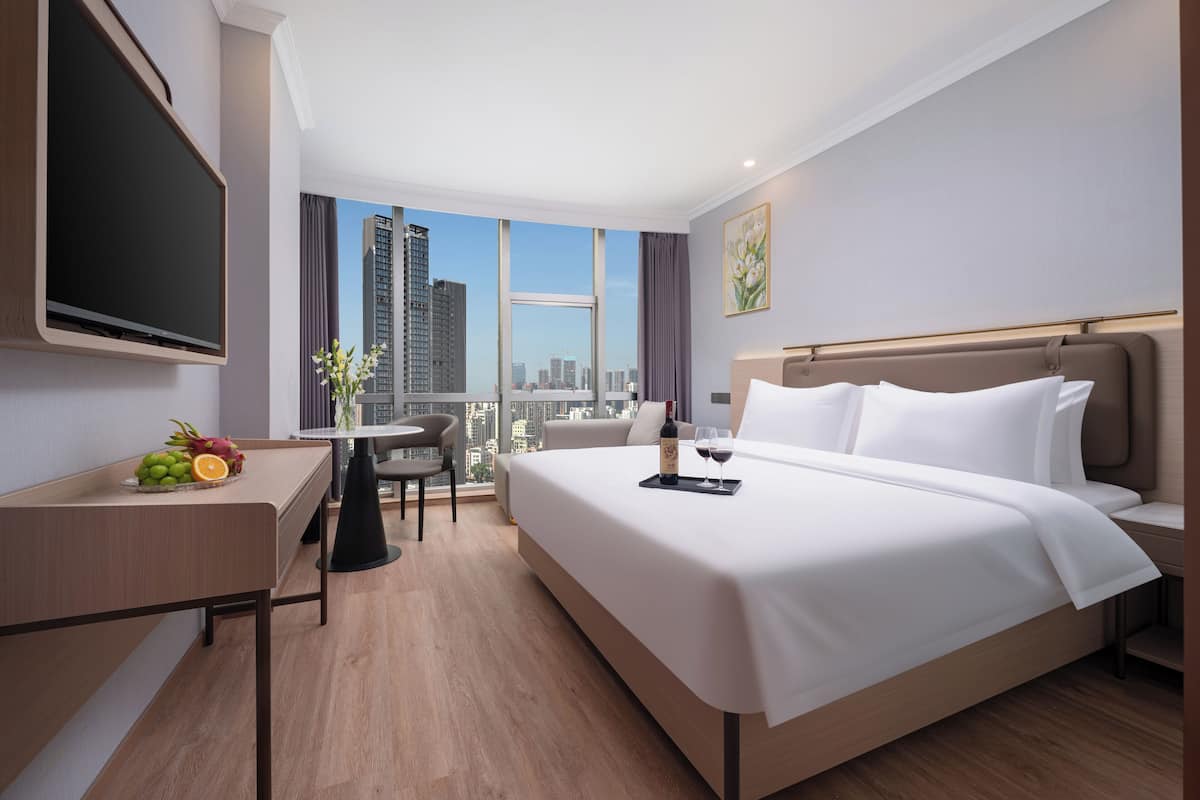 Habitación de hotel con una cama grande, un escritorio con televisor de pantalla plana, un comedor y vistas a la ciudad.