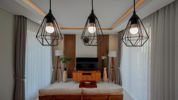Ein modernes Wohnzimmer mit Flachbildfernseher, Holz-Unterhaltungseinheit und drei geometrischen Pendelleuchten.