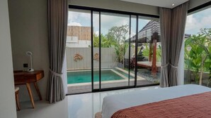 Ein Schlafzimmer mit einem großen Bett, einem Schreibtisch und Blick auf einen Swimmingpool und Außenbereich.