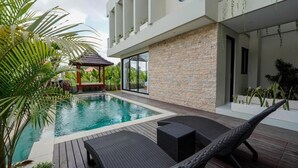 Ein moderner Poolbereich mit Holzterrasse, Liegestühlen und einer Steinwand.