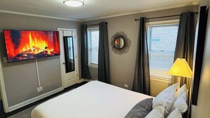 Une chambre d’hôtel avec un grand lit, un téléviseur à écran plat fixé au mur, une table de chevet avec une lampe et une fenêtre avec des rideaux.