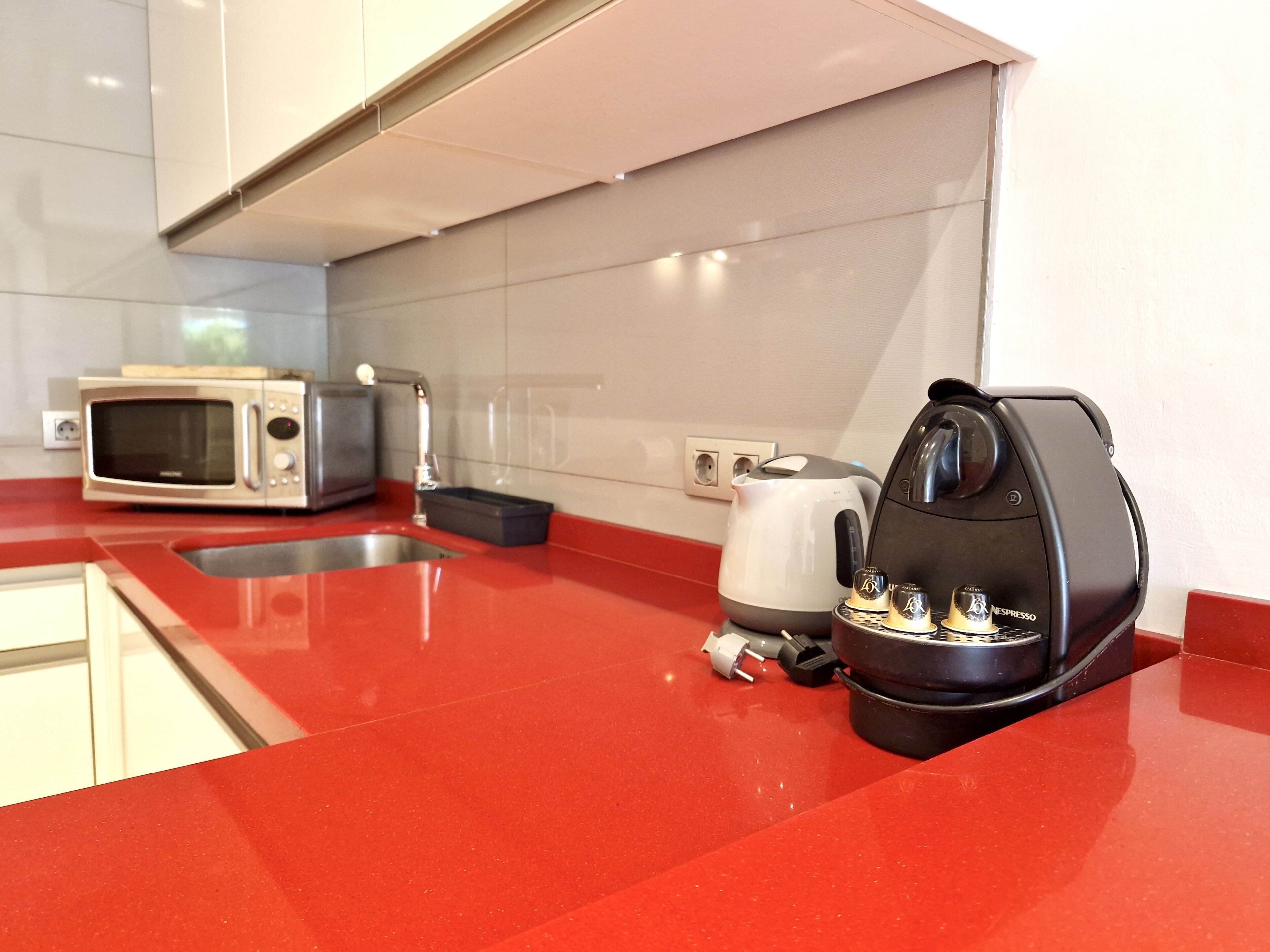Eine moderne Küche mit roter Arbeitsplatte, einer Mikrowelle, einem Toaster, einem Wasserkocher und einer Kaffeemaschine.