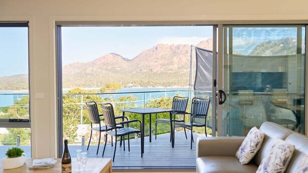 Ein Balkon mit Tisch und Stühlen, einer Couch und Blick auf Berge und Wasser.