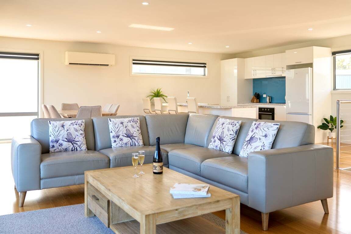 A modern living room with a grey sectional sofa, a wooden coffee table, and a dining area with a white table and chairs.