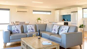 A modern living room with a grey sectional sofa, a wooden coffee table, and a dining area with a white table and chairs.