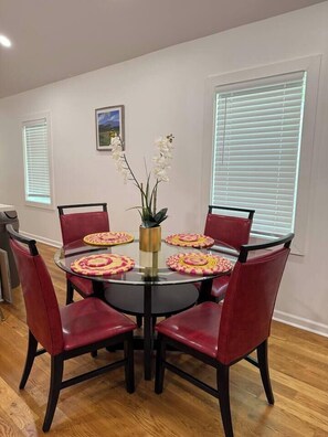 A dining area with a round glass table surrounded by six red chairs, a vase with white flowers, and a framed picture on the wall. - Safari Getaway: MBenz & Beltline (Atlanta)