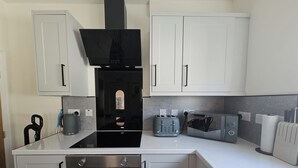 A compact kitchen with white cabinets, a black range hood, a built-in oven, a toaster, and a kettle.