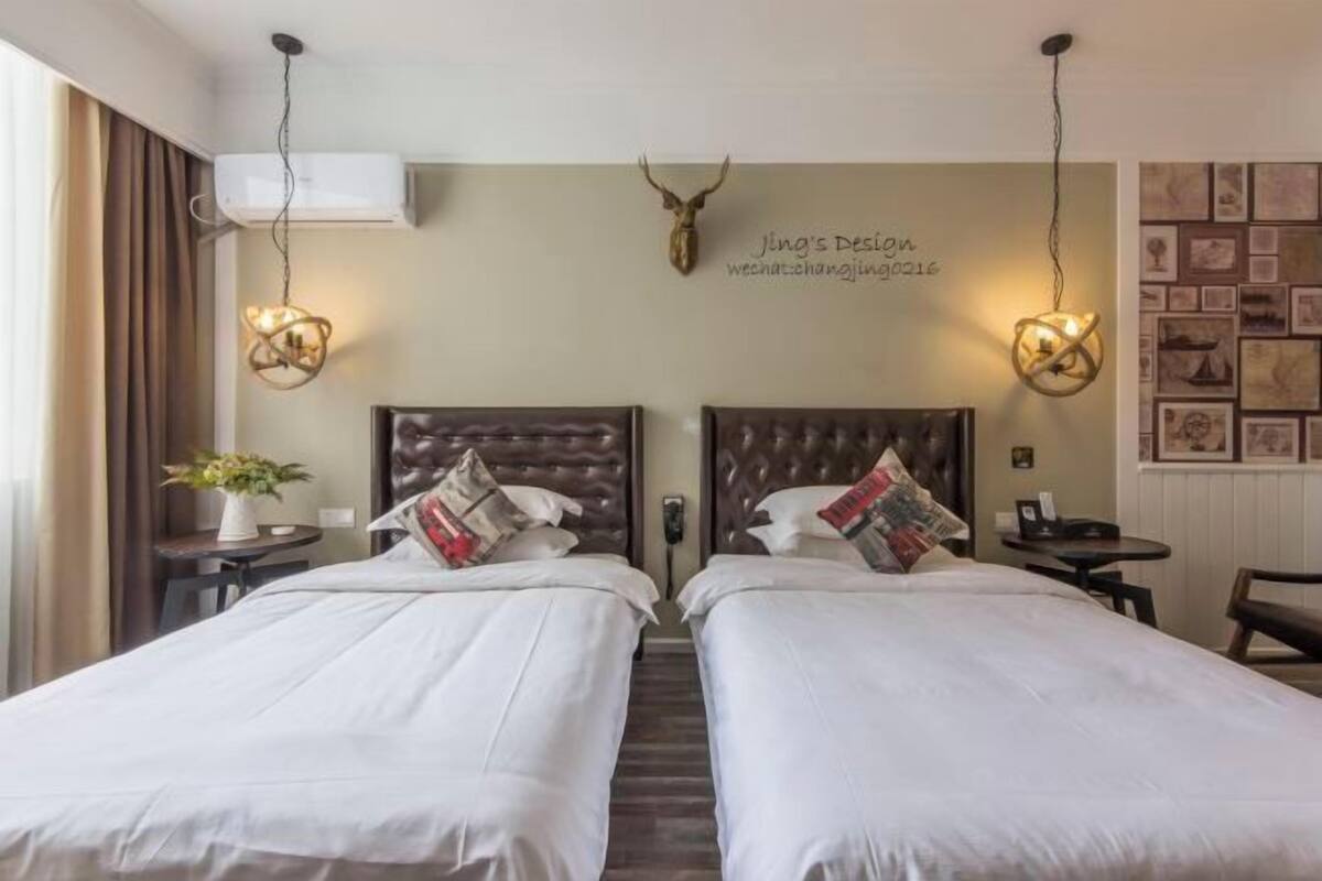 Habitación de hotel con dos camas, una cabeza de venado montada en la pared, luces fijas y un cuadro enmarcado.