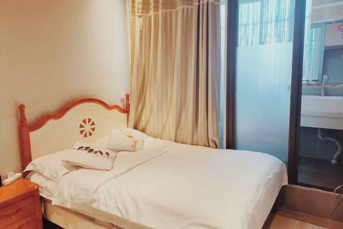 Una cama bien arreglada con tablero de madera, una almohada blanca y una mesita de noche con lámpara.