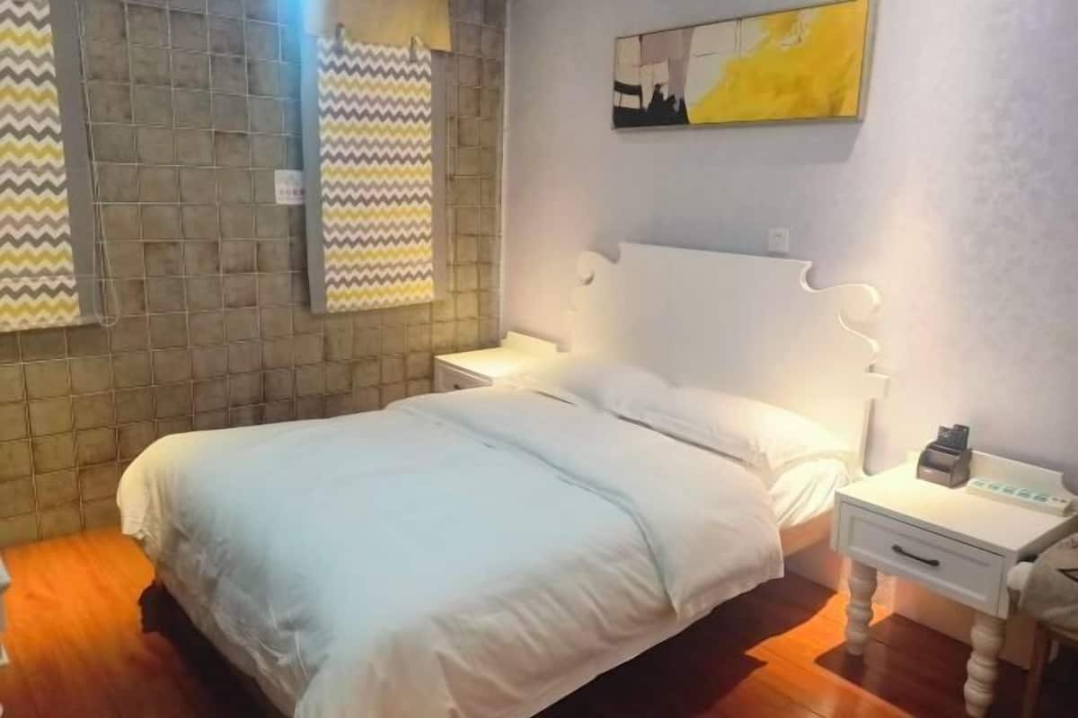 Un dormitorio con cama, mesita de noche, lámpara, una obra de arte colgada en la pared y cortina estampada.